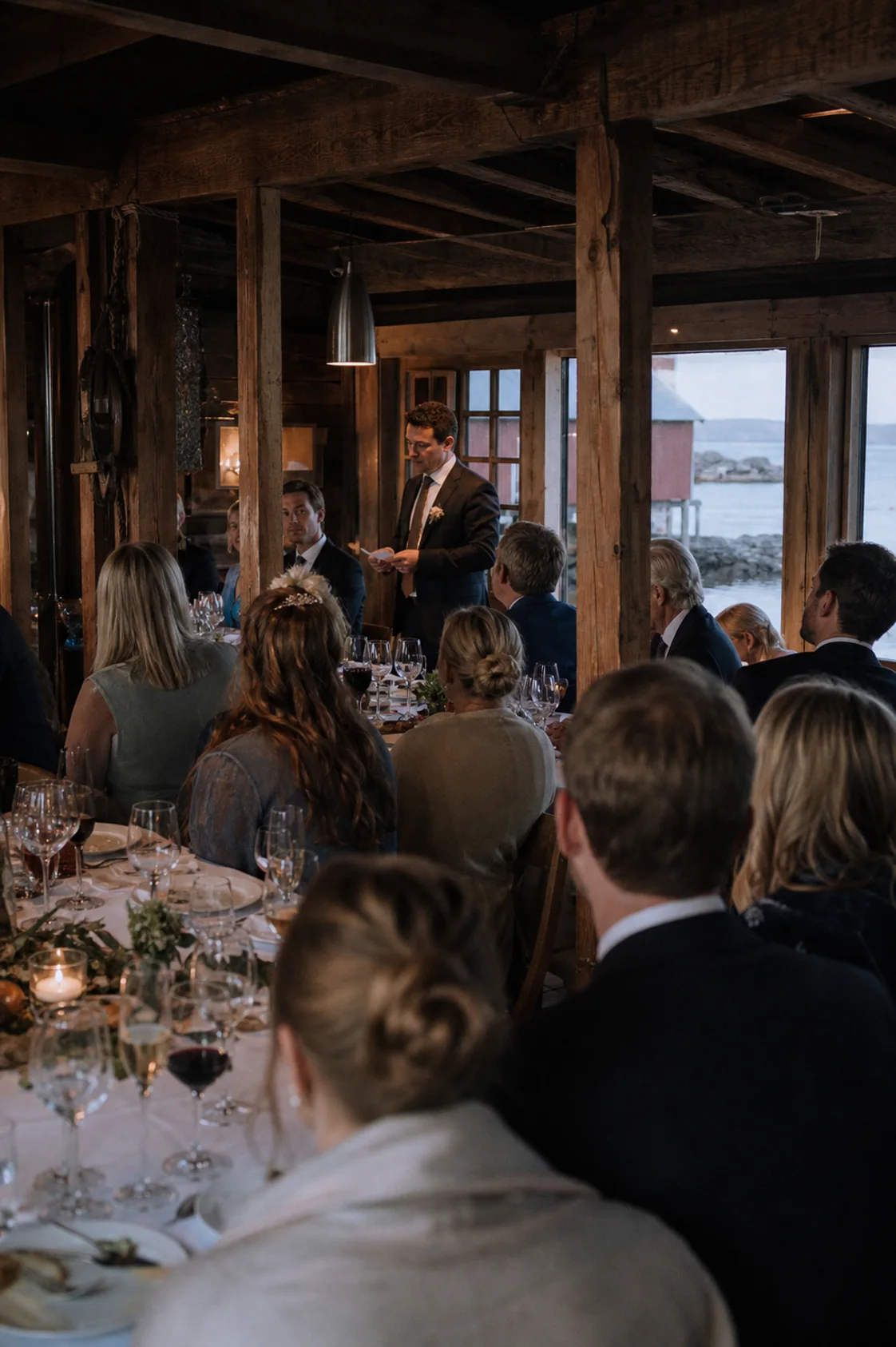 Bryllupsgjester lytter til en tale under middag i et naust